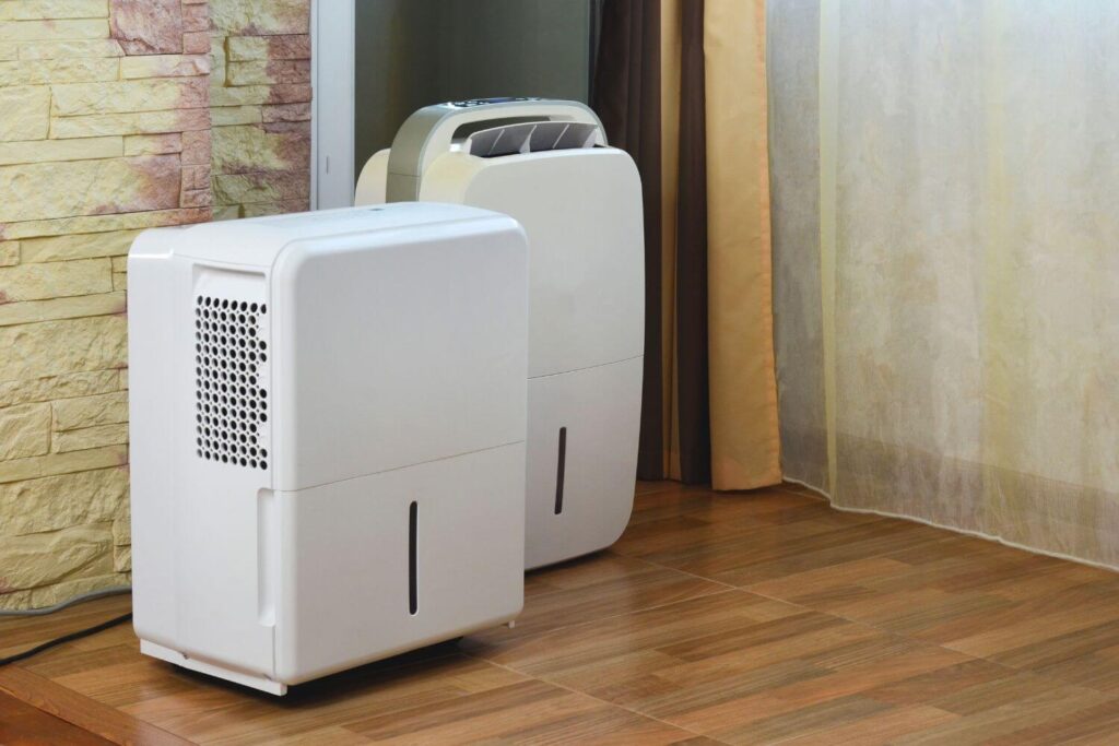 Two white dehumidifiers on the wood floor of a basement