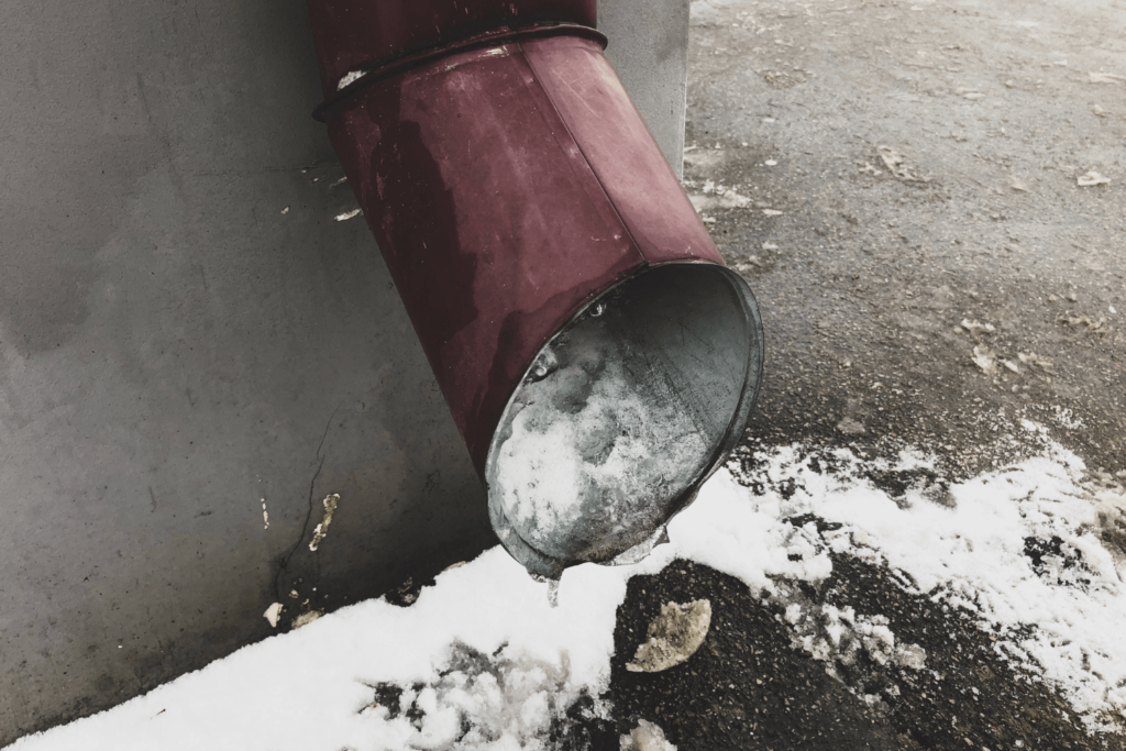 Gutter with frozen water pouring out from it.