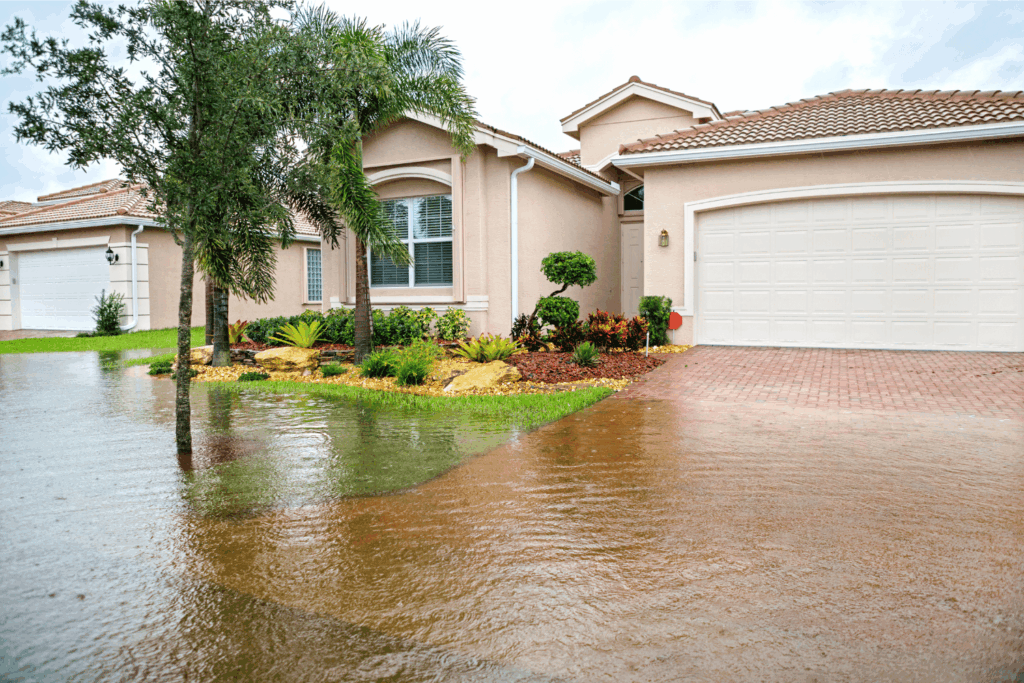A peach colored house with a paver driveway that is flooded almost to the entrance of the garage