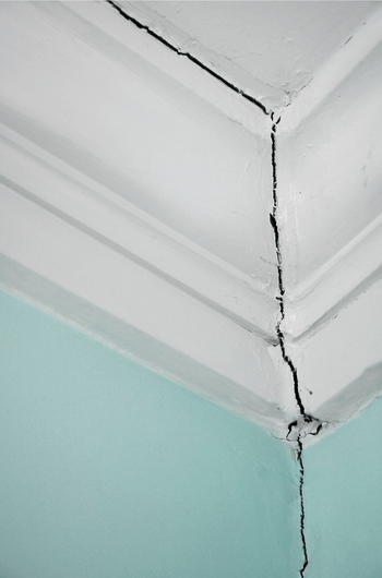 an inside wall of a home with teal wall paint and white crown molding exposing a crack from the ceiling down to the wall