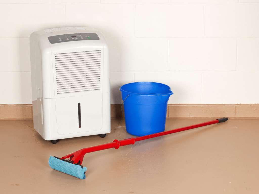 a white dehumidifier is sitting on a basement floor next to a blue bucket and a red mop