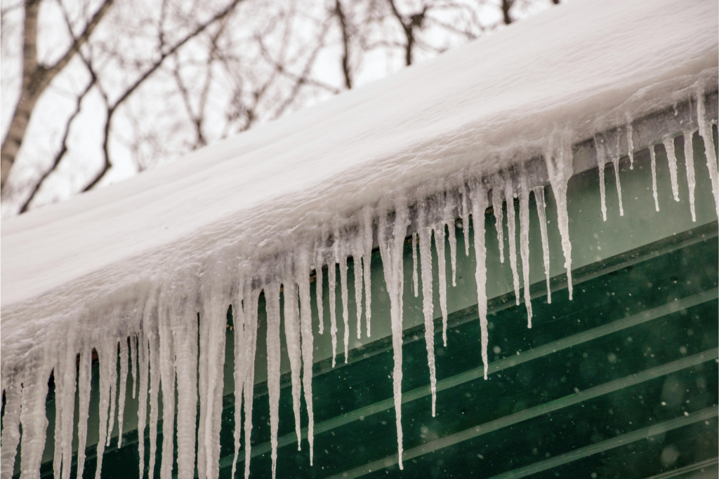 Roofline of a home with icicles and snow on its roof.